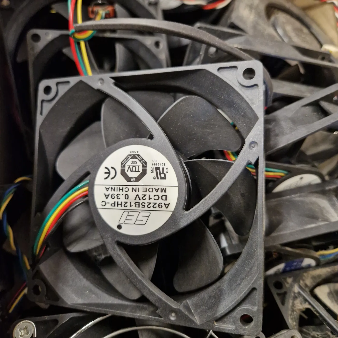 Ventilateur 12 V récupéré, étiquette Made in China visible, dans un bac de pièces de l'association RACK