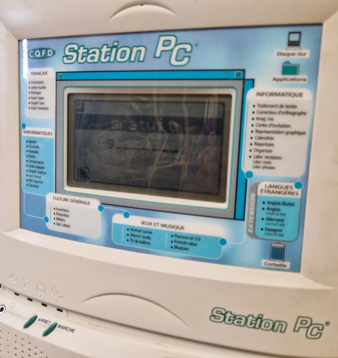 Gros plan sur l'écran de la Station PC : écran LCD monochrome au centre, entouré du menu imprimé des rubriques Français, Mathématiques, Culture générale, Jeux et musique, Informatique et Langues étrangères